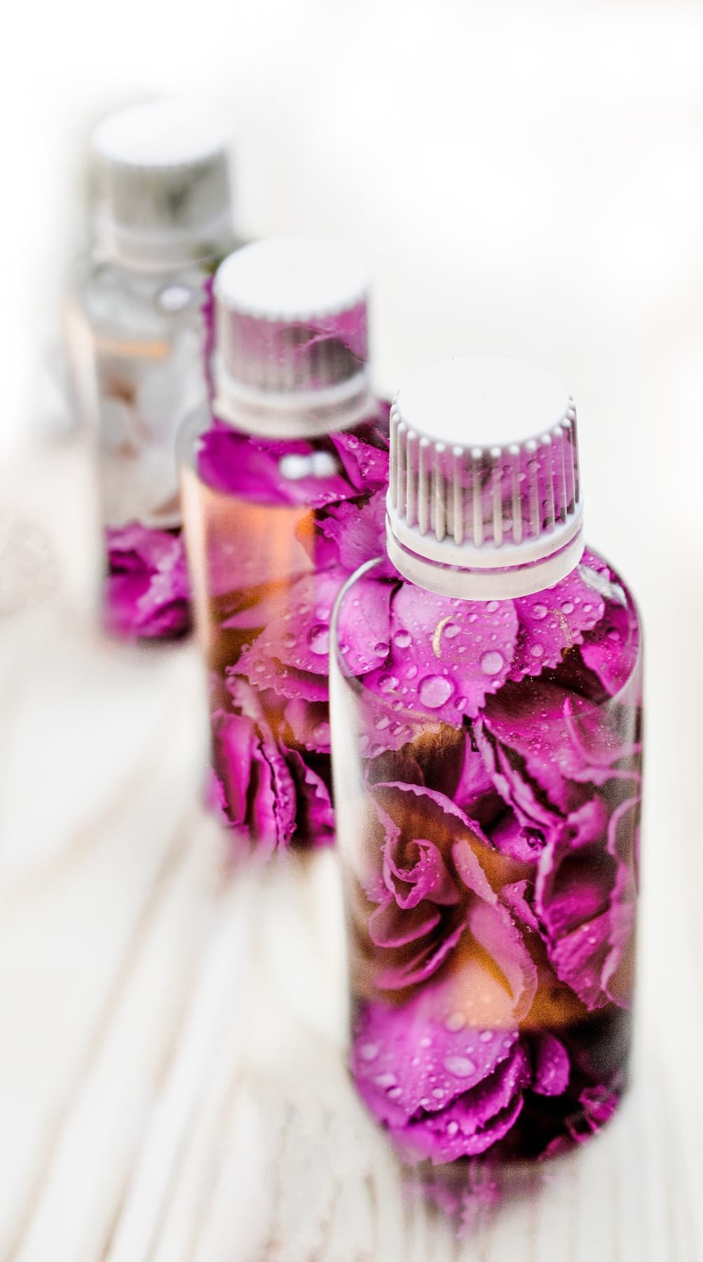 Ätherische Öle mit Blüten in klaren Glasflaschen